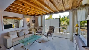 A modern living room with a glass coffee table, two floral armchairs, a sofa, and a TV. - Skol 212. Two Bedrooms Duplex in Marbella Centre on the Beachfront. (Marbella)