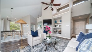 A spacious living room with a ceiling fan, a glass coffee table, and a white sofa with blue cushions. - Orchid On The Water - w/ Boat Slip On Lake Hamilton! (Hot Springs)