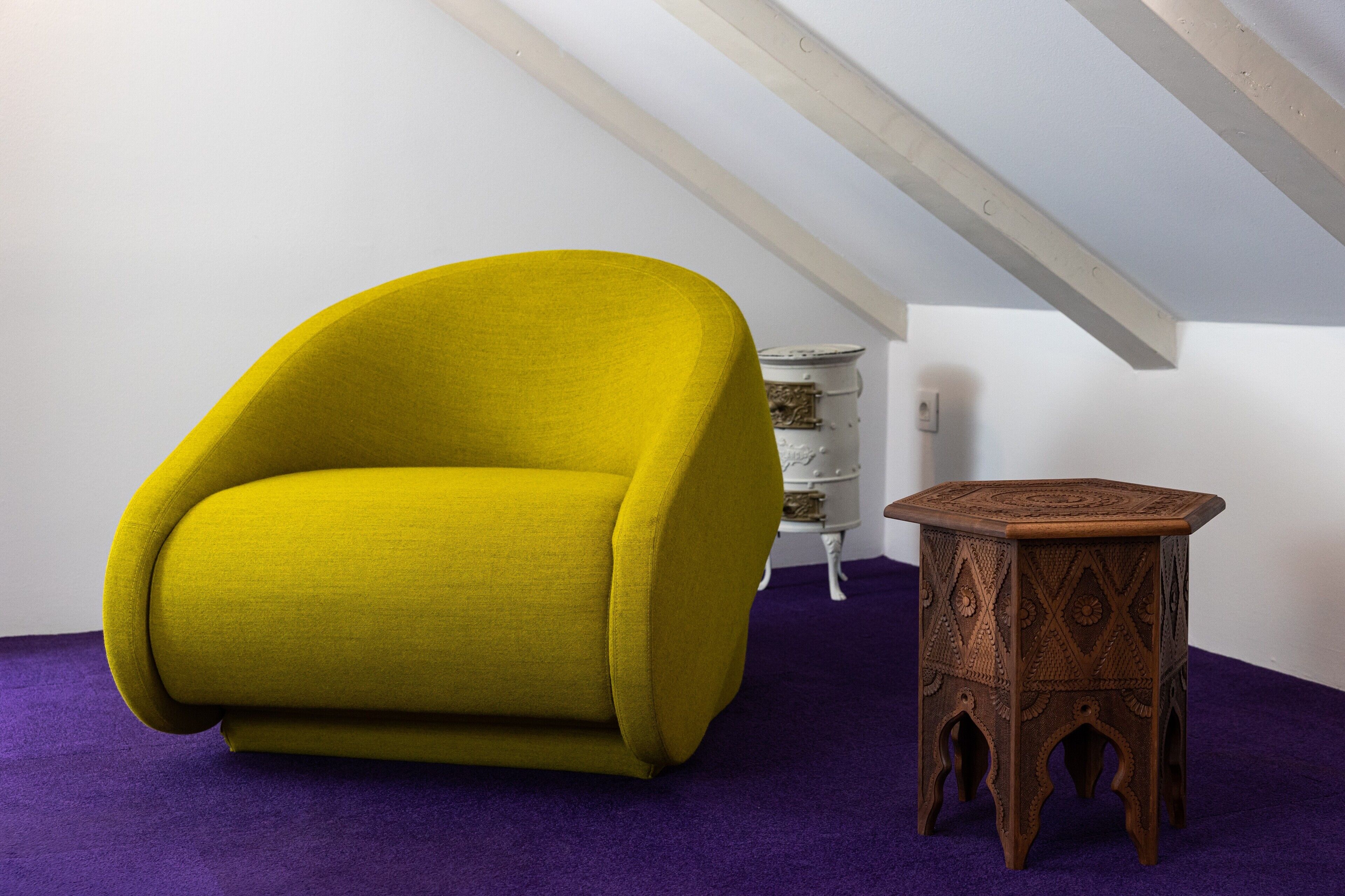 A room with a yellow armchair, a small wooden side table, and a purple carpet.