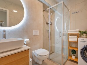 Features a sleek mirror, vessel sink, toilet, and glass-enclosed shower.