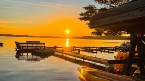 Solnedgang over et stille søområde med fortøjede både og en bænk.