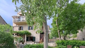 A two-story house with a stone facade, a balcony, and a well-maintained garden with grass, shrubs, and a tree. - Authentic Stone House Lola (Makarska)