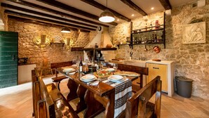 A rustic dining area with a stone wall, wooden beams, and a wooden table set for a meal. - Authentic Stone House Lola (Makarska)