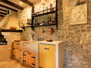 Cozy kitchen with a stone wall backdrop, featuring a wooden cabinet, copper pot, and wooden stool.