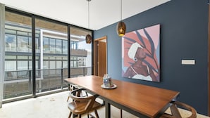 Un espace de repas moderne avec une table et des chaises en bois, une grande peinture abstraite au mur et une vue sur la ville à travers de grandes fenêtres.