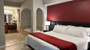 Ein Hotelzimmer mit einem großen Bett, einer roten Akzentwand, einem eigenen Badezimmer mit Waschtisch und einem Spiegel.