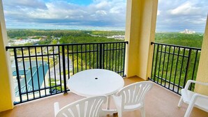 Ein Balkon mit rundem Tisch und zwei Stühlen, der auf eine grüne Landschaft und ein Gewässer blickt.