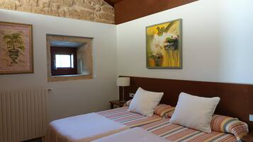 Habitació d'hotel amb dos llits, una finestra, un radiador i un quadre penjat a la paret.