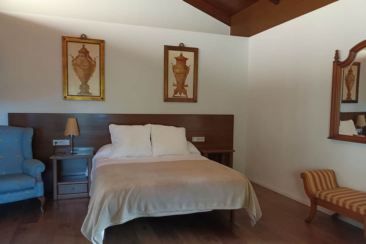 A bedroom with a bed, a nightstand, a lamp, a chair, and two wall-mounted paintings.