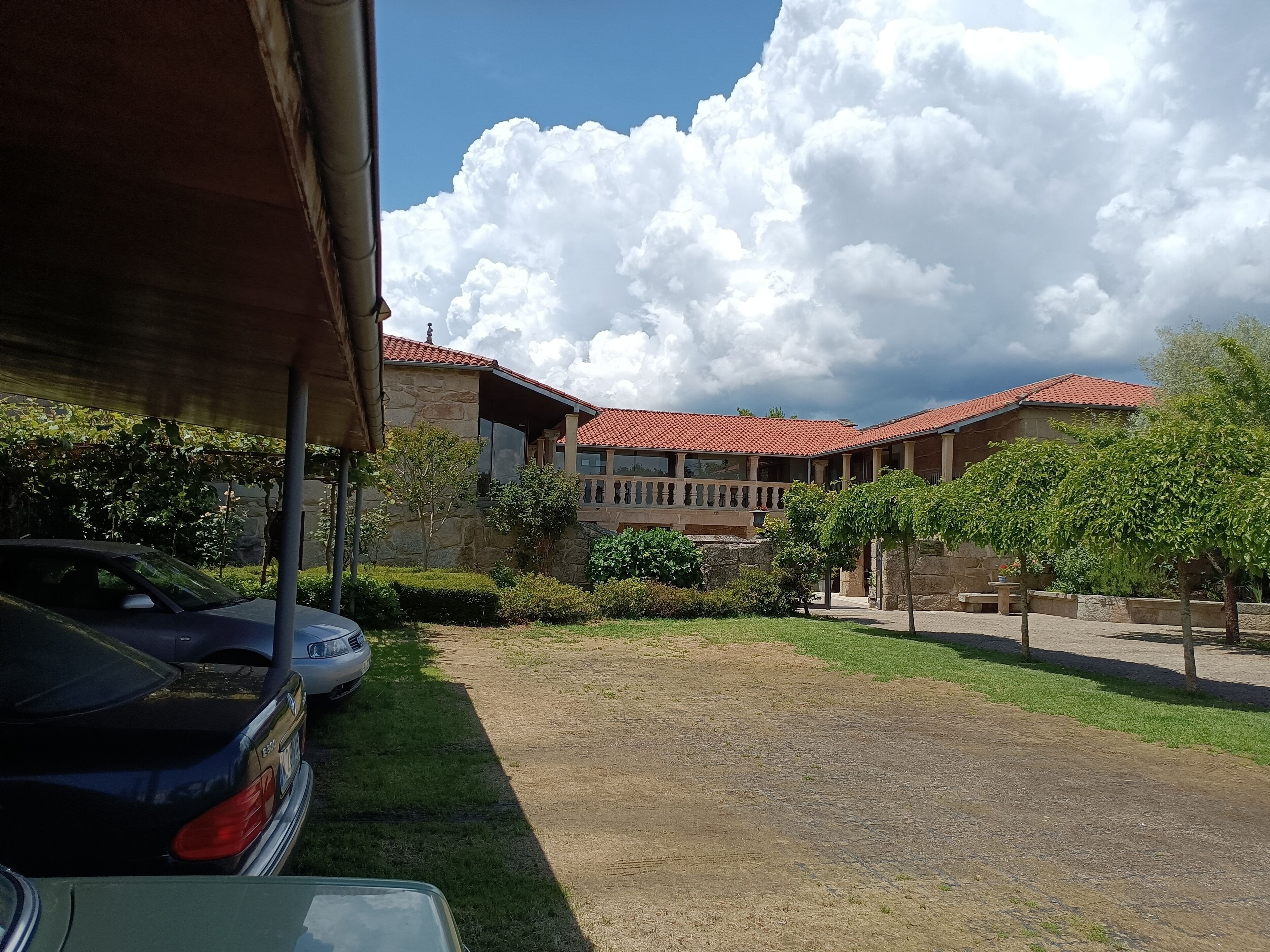 Un patio con un edificio de piedra, coches aparcados y cielo despejado.