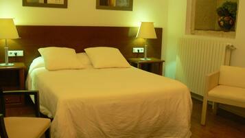 Una cama bien hecha con sábanas blancas en una habitación de hotel. Hay dos mesitas de noche con lámparas, una silla y una ventana con vistas al exterior.