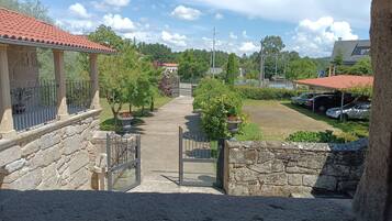 A stone pathway leading to a gated entrance with a view of a parking area and buildings in the background.