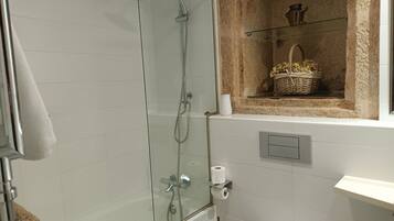 A modern bathroom with a glass-enclosed shower, a toilet, and a shelf with a basket.