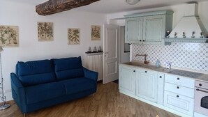 Un salon chaleureux avec un canapé bleu, un radiateur blanc et une cuisine dotée de meubles bleu clair et d’un pare-feu blanc.