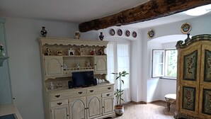 Une pièce comprenant un grand meuble en bois, un téléviseur posé sur un meuble, une plante en pot et une fenêtre avec des rideaux.