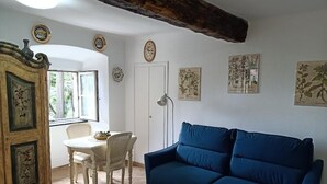 Une pièce avec un canapé bleu, un meuble en bois orné de motifs floraux, une table blanche avec des chaises et des œuvres d’art murales sur le thème de la botanique.