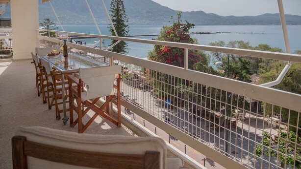 A balcony with a table and chairs, overlooking a body of water and mountains. - Seafront Apartment Grace (Kalamata)