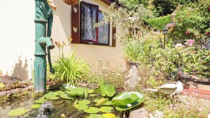Een tuin met een vijver, een huis met een raam en diverse planten.