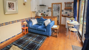 Een gezellige woonkamer met een blauwe bank, een geruit vloerkleed en een eethoek met een tafel en stoelen.