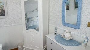 Een slaapkamer met een witte garderobe, een dressoir, een spiegel en bloemenbehang.