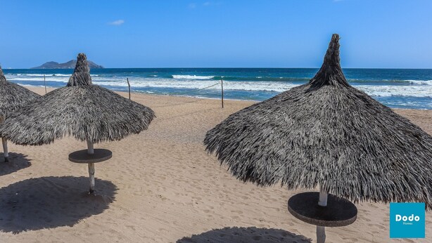 Una playa con sombrillas de techo de paja y una vista despejada del océano.