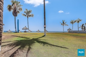 A beach area with palm trees, a thatched-roof structure, and a clear blue sky.