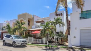 Una calle residencial con casas modernas, un coche blanco estacionado al lado y una valla de piquetes blancos.