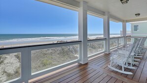 A wooden deck with rocking chairs overlooking a beach.