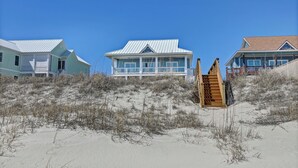 A beachfront property with a wooden staircase leading to a house with a white roof and blue windows.