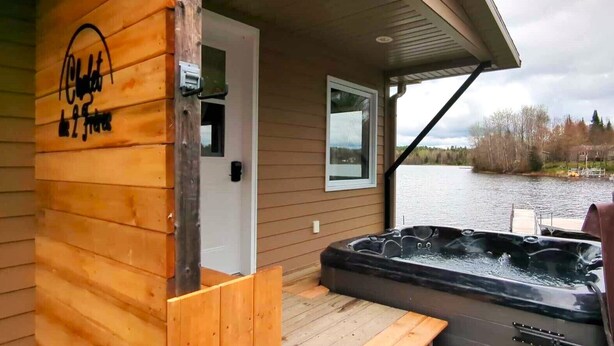 A wooden cabin with a hot tub and a view of a lake.
