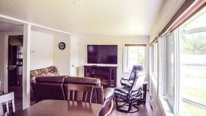 A spacious living room with a fireplace, a television, and a large window offering a view of the outdoors.