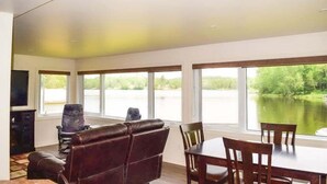 A spacious living room with a large window overlooking a lake, a fireplace, and a dining area with wooden furniture.