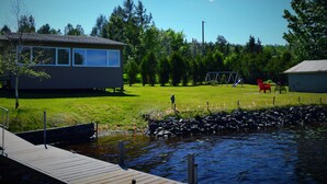 A lakeside property with a dock, a small building, a swing set, and a red chair.