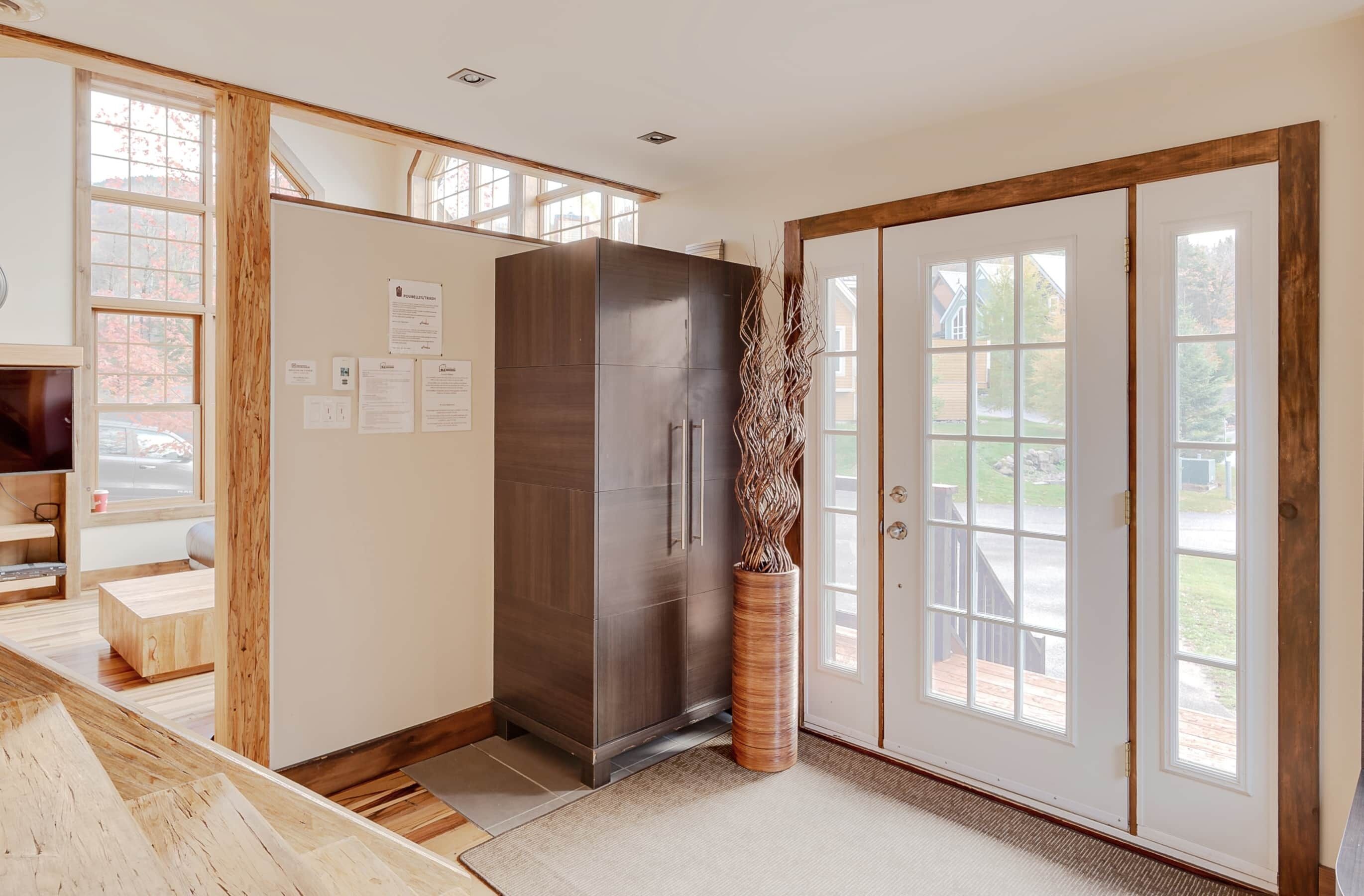 A modern kitchen with a large dark-colored refrigerator, wooden cabinets, and a large window.