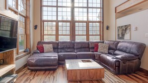 A spacious living room with a large sectional sofa, a wooden coffee table, and a large window with multiple panes. - Le Morgan - In Stoneham (Stoneham-et-Tewkesbury)
