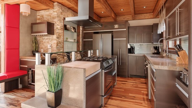 A modern kitchen with a central island, stainless steel appliances, and a stone accent wall. - Le Morgan - In Stoneham (Stoneham-et-Tewkesbury)