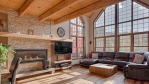 A spacious living room with a stone fireplace, leather sofa, and large windows. - Le Morgan - In Stoneham (Stoneham-et-Tewkesbury)