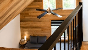 Un intérieur en bois avec un plafond en pente, un ventilateur de plafond, une fenêtre et un escalier.