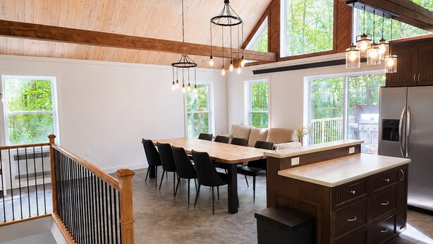 Une cuisine spacieuse avec un plafond en bois, de grandes fenêtres et un coin repas comprenant une table et des chaises.