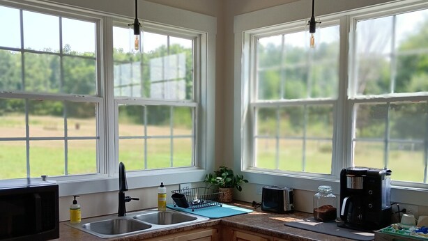 Cocina con armarios de madera, microondas, pileta y cafetera. Se ven ventanas con vista a zonas verdes.