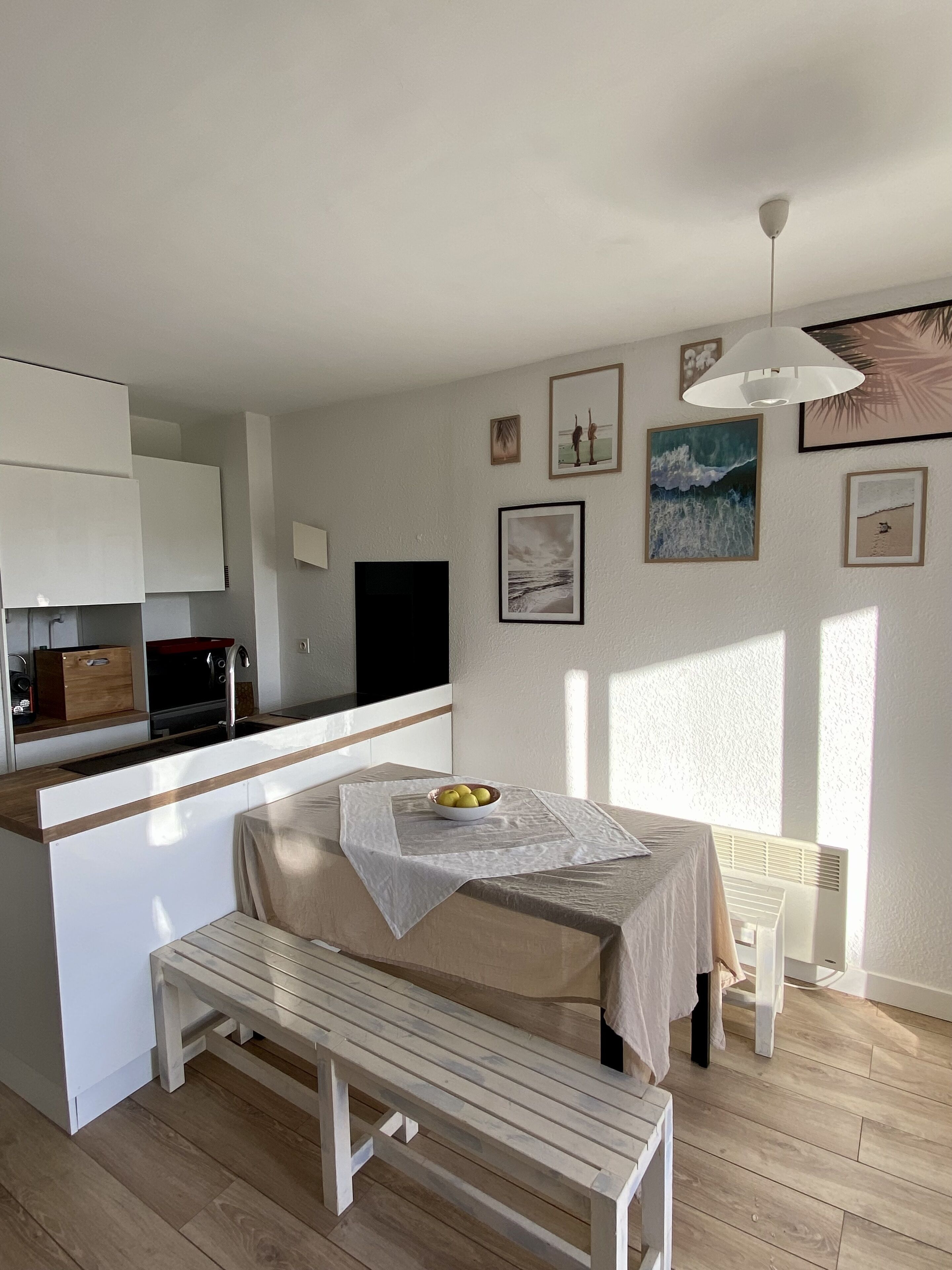 A modern kitchen with white cabinets, a dining area with a bench and table, and a small island with a bowl of fruit.