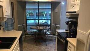 Una cocina con piso de baldosas de piedra, armarios blancos, una mesa de comedor con sillas y vistas a través de una ventana.