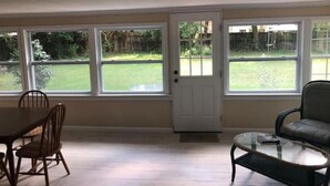 Una habitación con una mesa de comedor y sillas, un sofá, y ventanas amplias que ofrecen vistas a un patio.