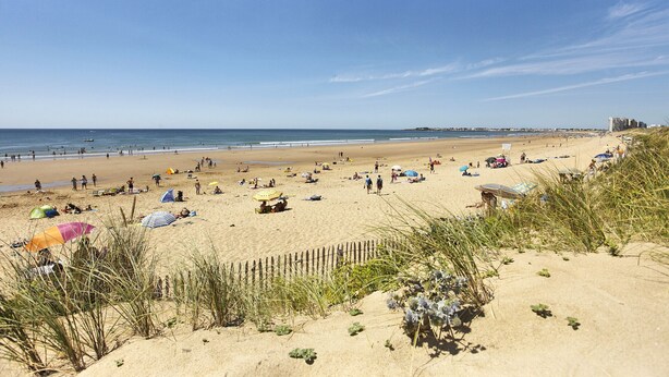Une plage de sable où l’on voit des gens, des parasols et une clôture en bois.
