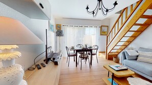 Un salon chaleureux avec un coin repas, un escalier en bois et un téléviseur placé à gauche.