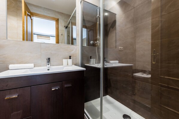 Un baño moderno con ducha de vidrio, tocador con espejo y un espejo grande sobre el lavabo.