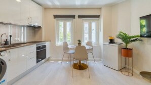 A modern kitchen with white cabinets, a dining table with chairs, and a coffee machine. - Bonneville Setúbal II (Setúbal)