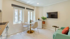 A modern living room with a dining area, a flat-screen TV mounted on the wall, and a green sofa with orange cushions. - Bonneville Setúbal II (Setúbal)