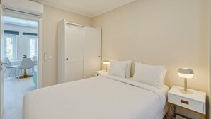 A hotel room with a large bed, bedside tables with lamps, a wardrobe, and a view of a dining area. - Bonneville Setúbal II (Setúbal)