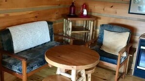 A cozy cabin interior with a wooden floor, a sofa, a chair, and a small wooden table.